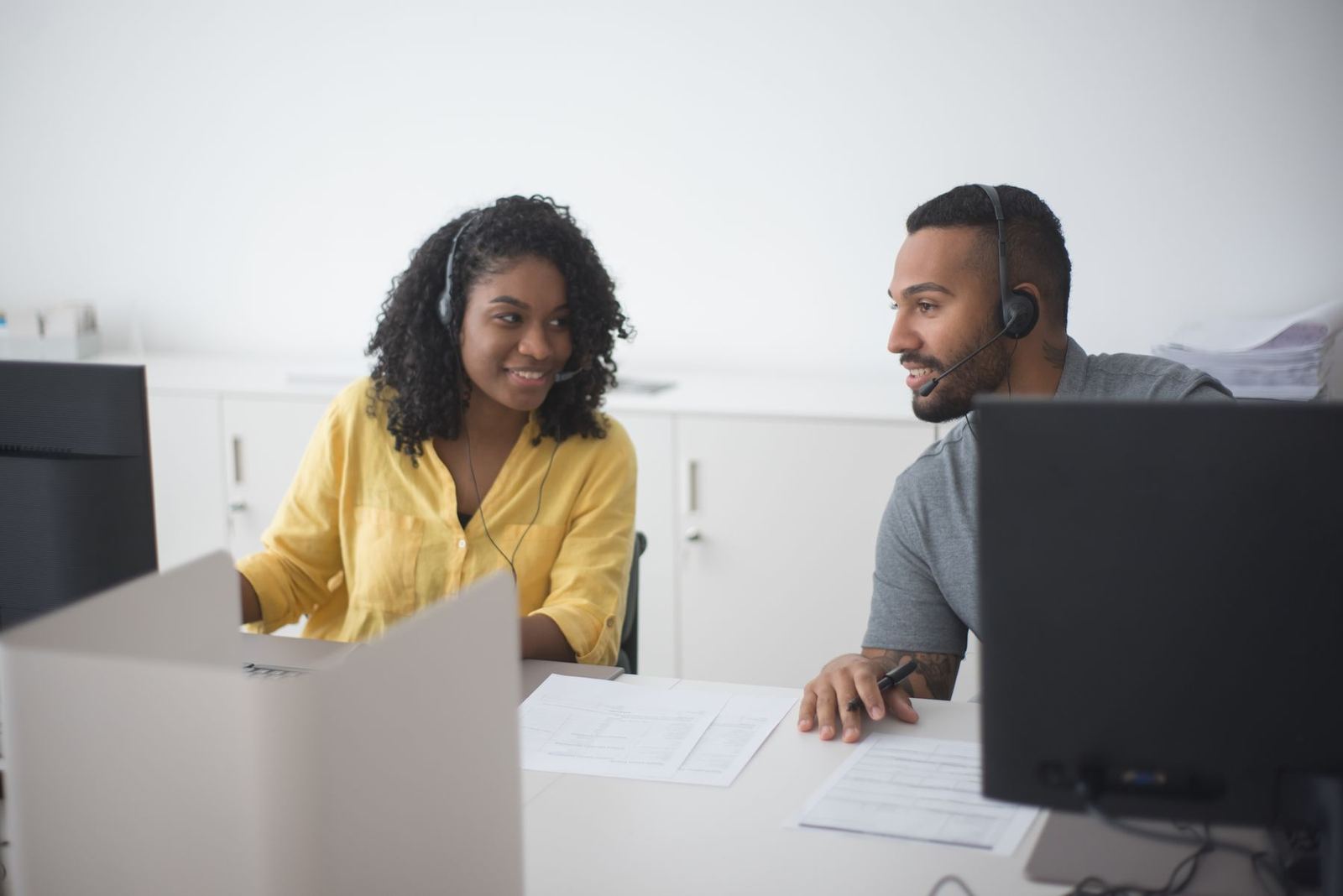 Two call center agents on headsets talking at their desks