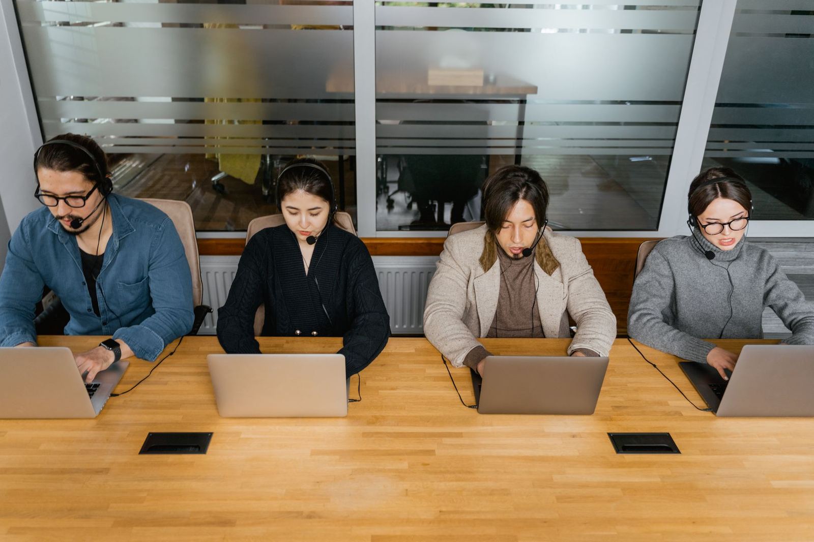 Call center agents in headsets working at laptops, seen from above