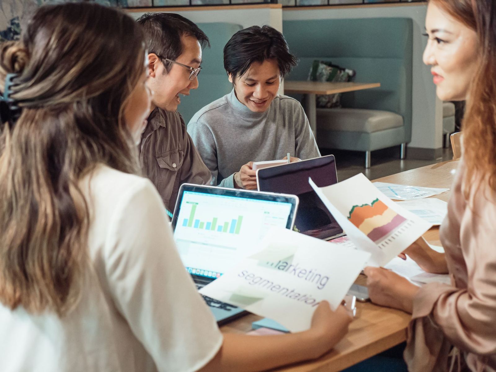 Marketing team discussing campaign charts and printed plans around a laptop
