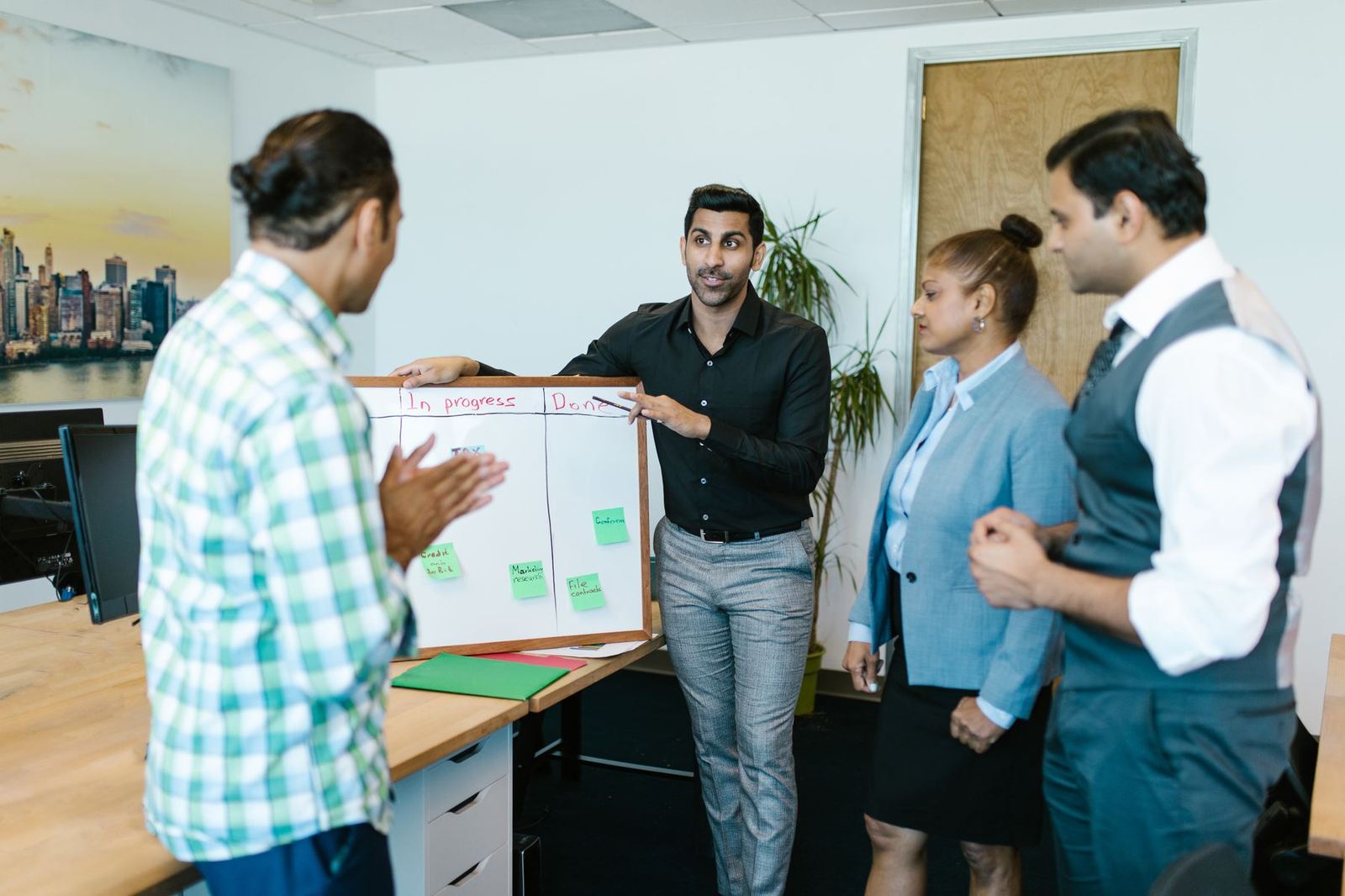 A small team standing around a whiteboard of tasks, talking through the work