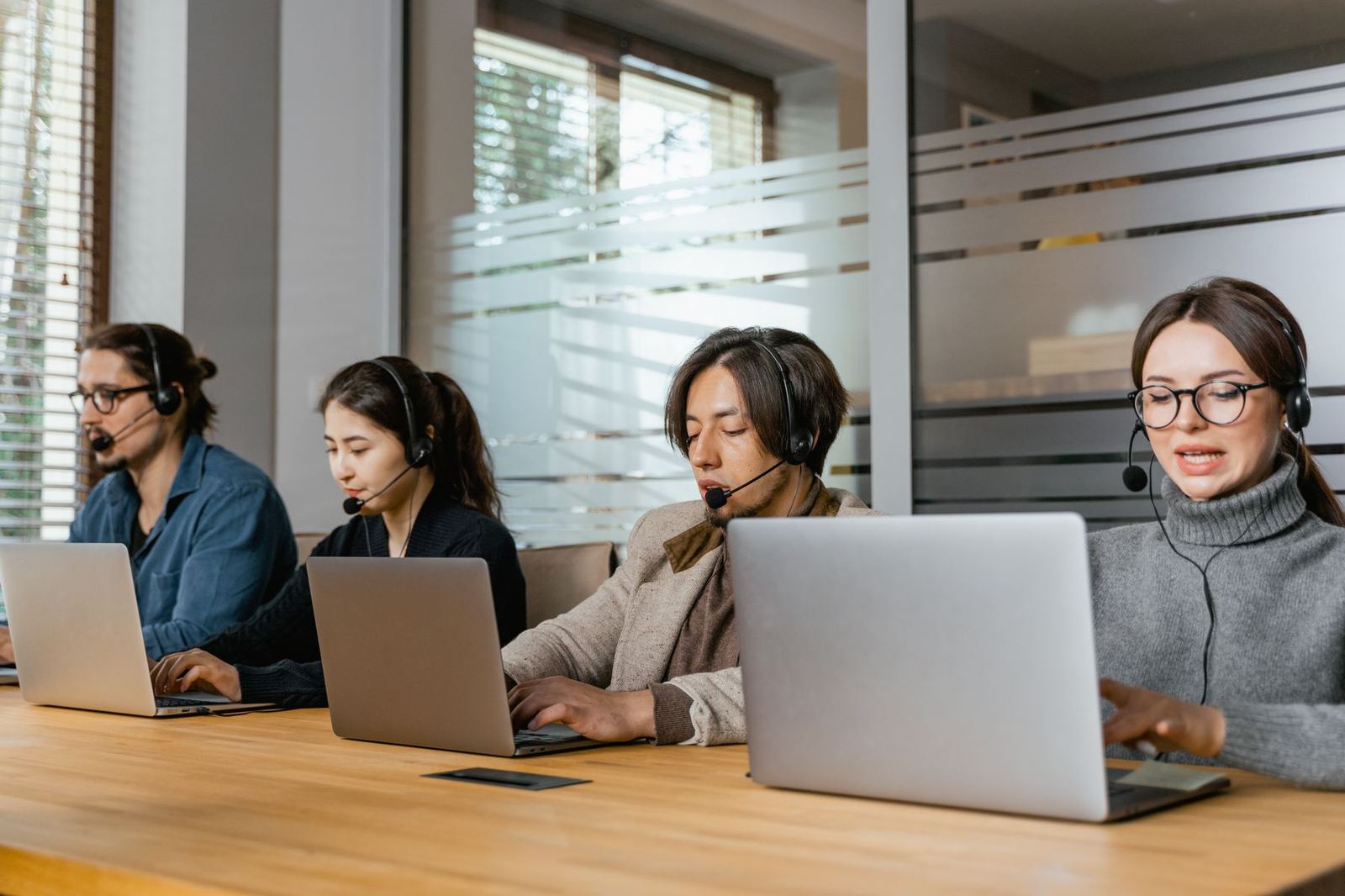 Call center agents on headsets working at laptops along a long wooden desk